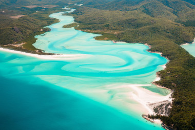 An iconic view of the Whitsundays in Queensland showing a vegetated landscape leading down to turquoise waters and white sand.