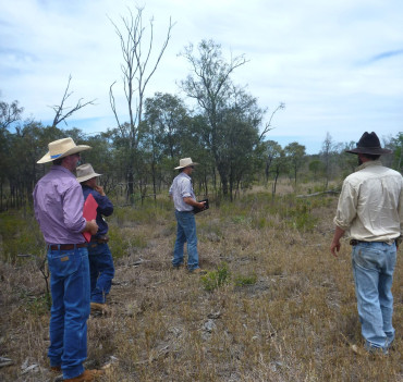 A group of people standing in a dry vegetated landscape looking outwards.